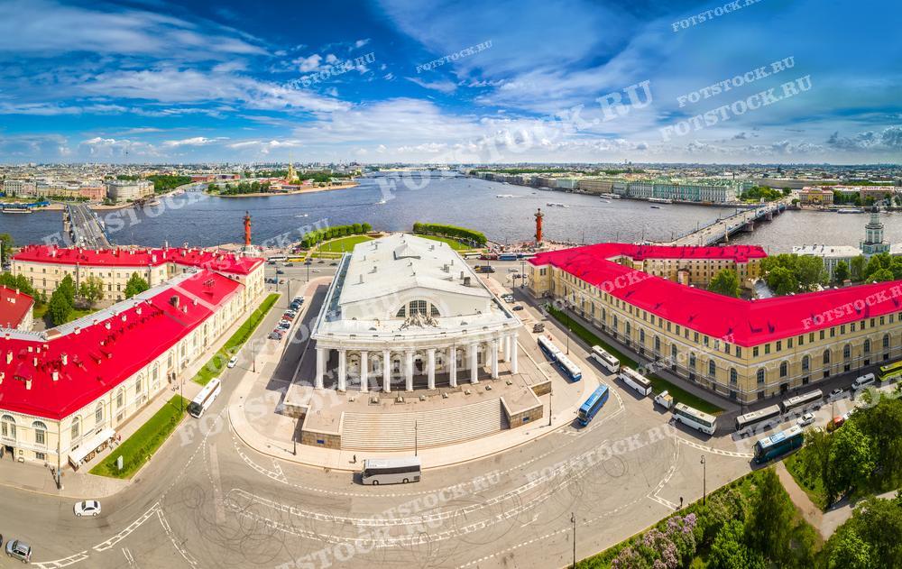 На фотографии изображён вид на исторический центр Санкт-Петербурга с воздуха.  Яркое солнечное освещение подчеркивает контраст красных крыш зданий и бирюзового оттенка водной поверхности. 
Это фото подходит для использования в качестве рекламного материала для туристических агентств, обложек путеводителей по городу, а также может быть использовано в образовательных и исследовательских целях.